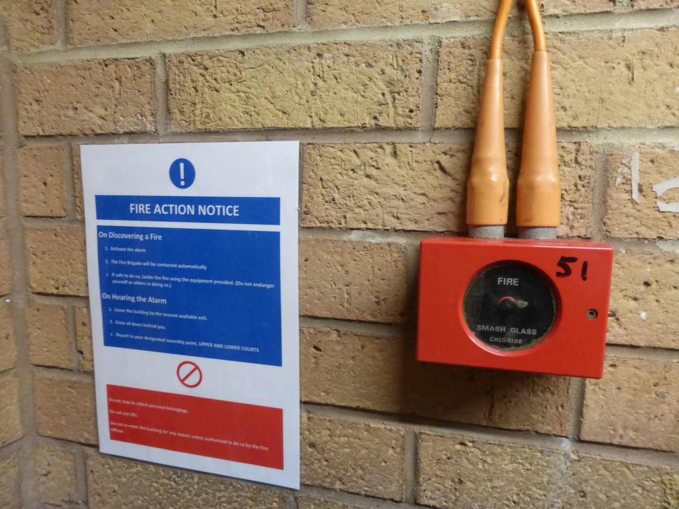 Red manual call point on wall with fire action notice