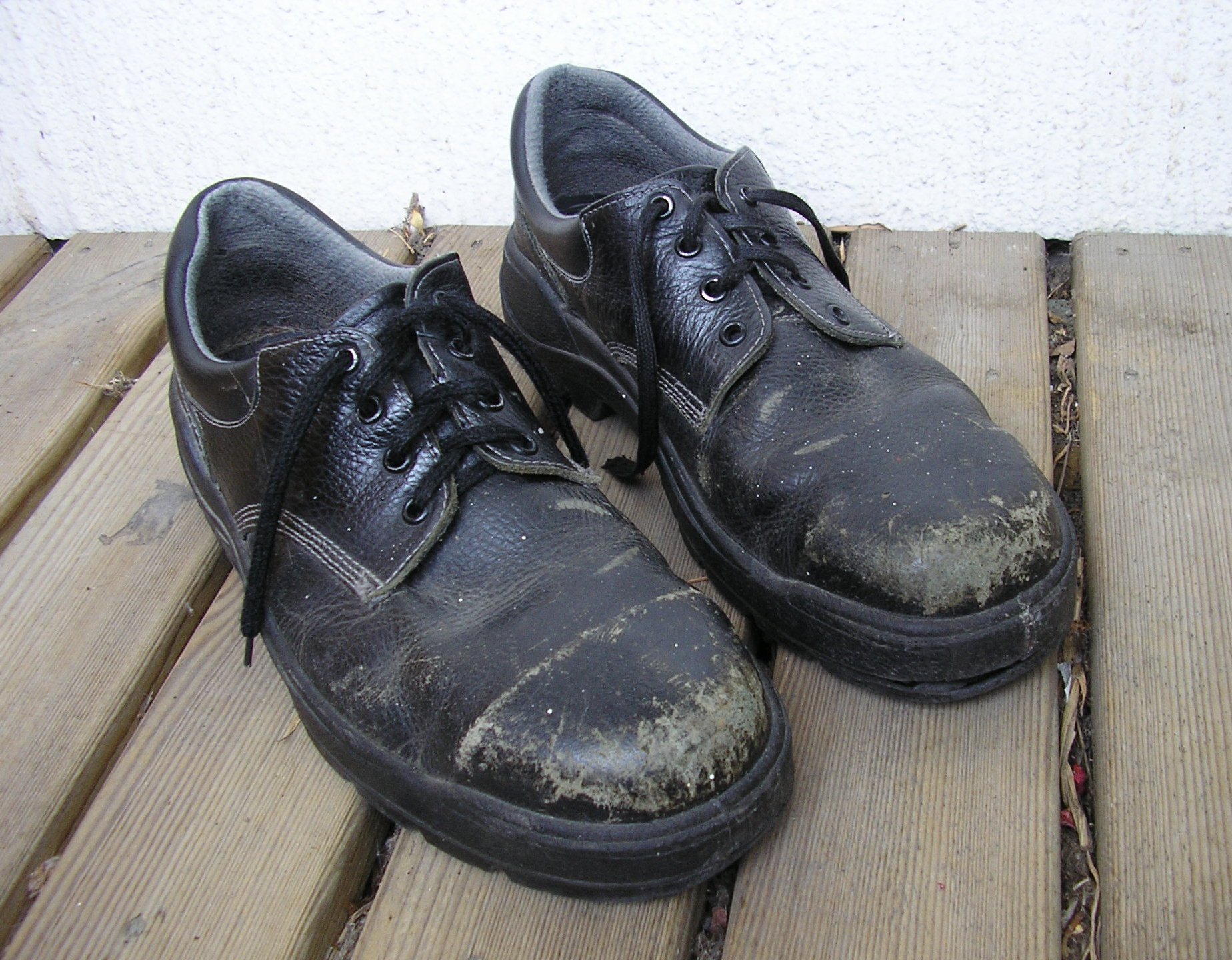 worn black safety boots on wooden floor