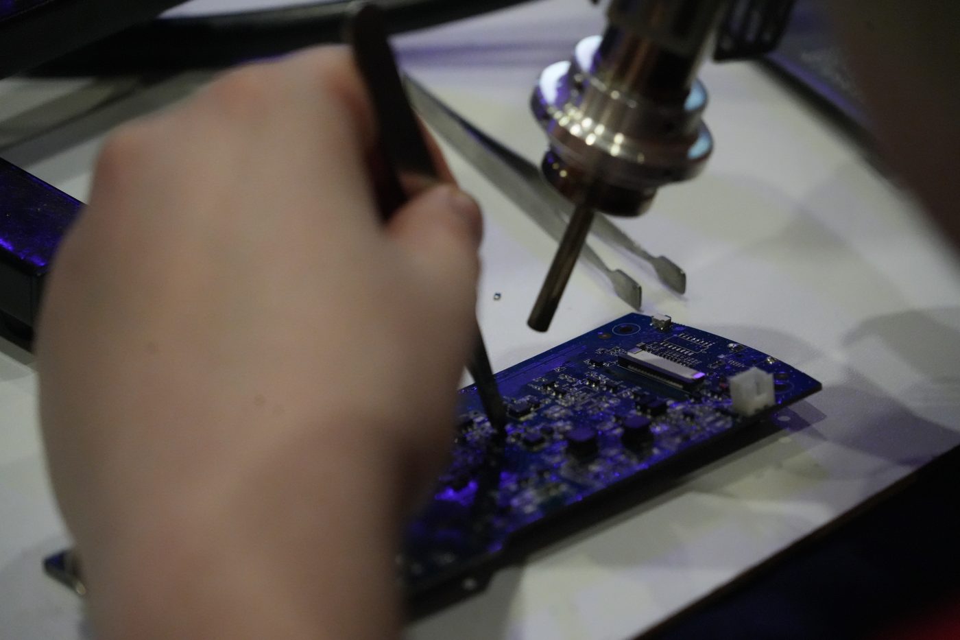 Hand holding tweezers near electronic circuit board